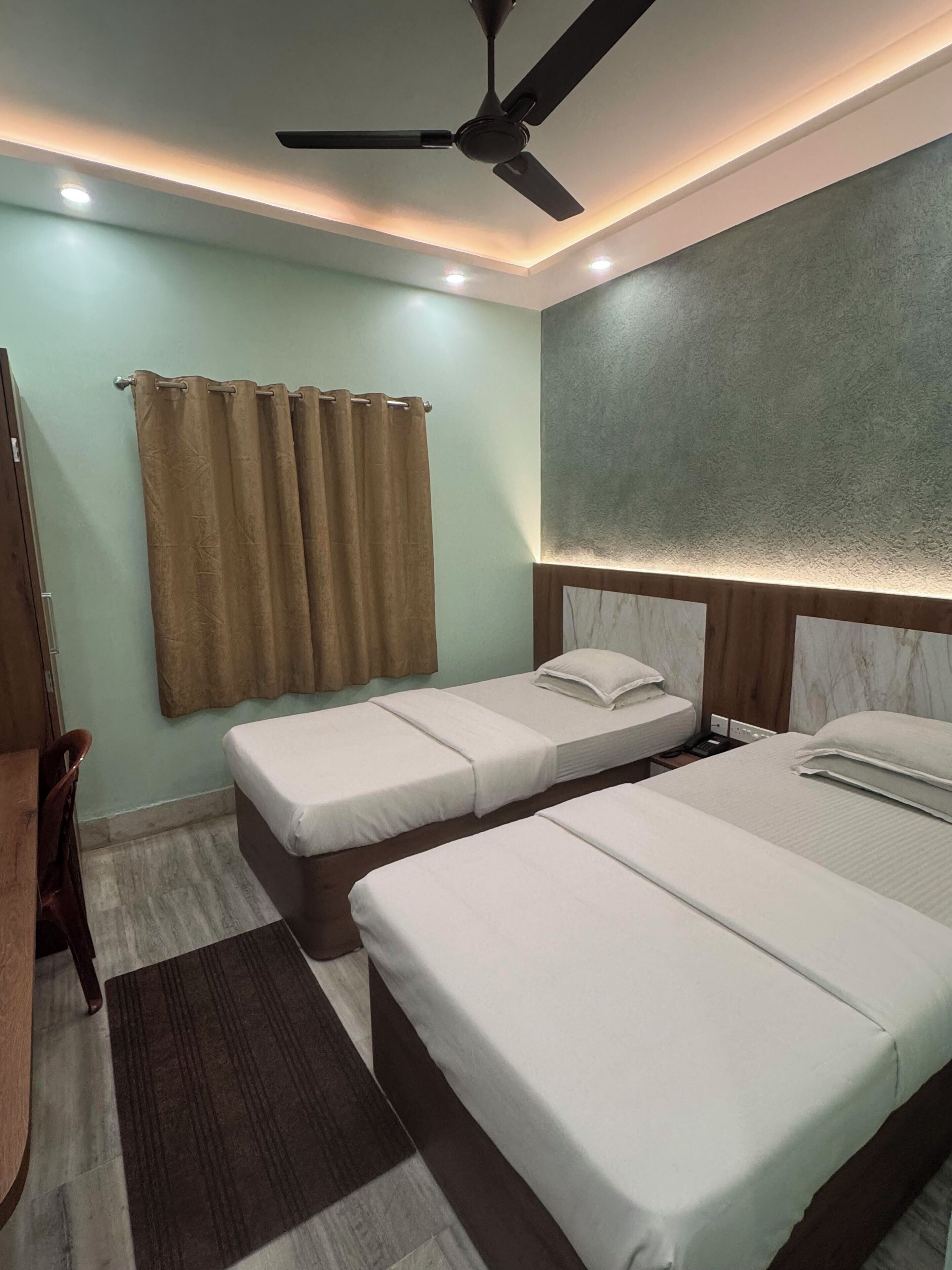 A hotel room with two beds, a ceiling fan, a window with curtains, and a wooden headboard.