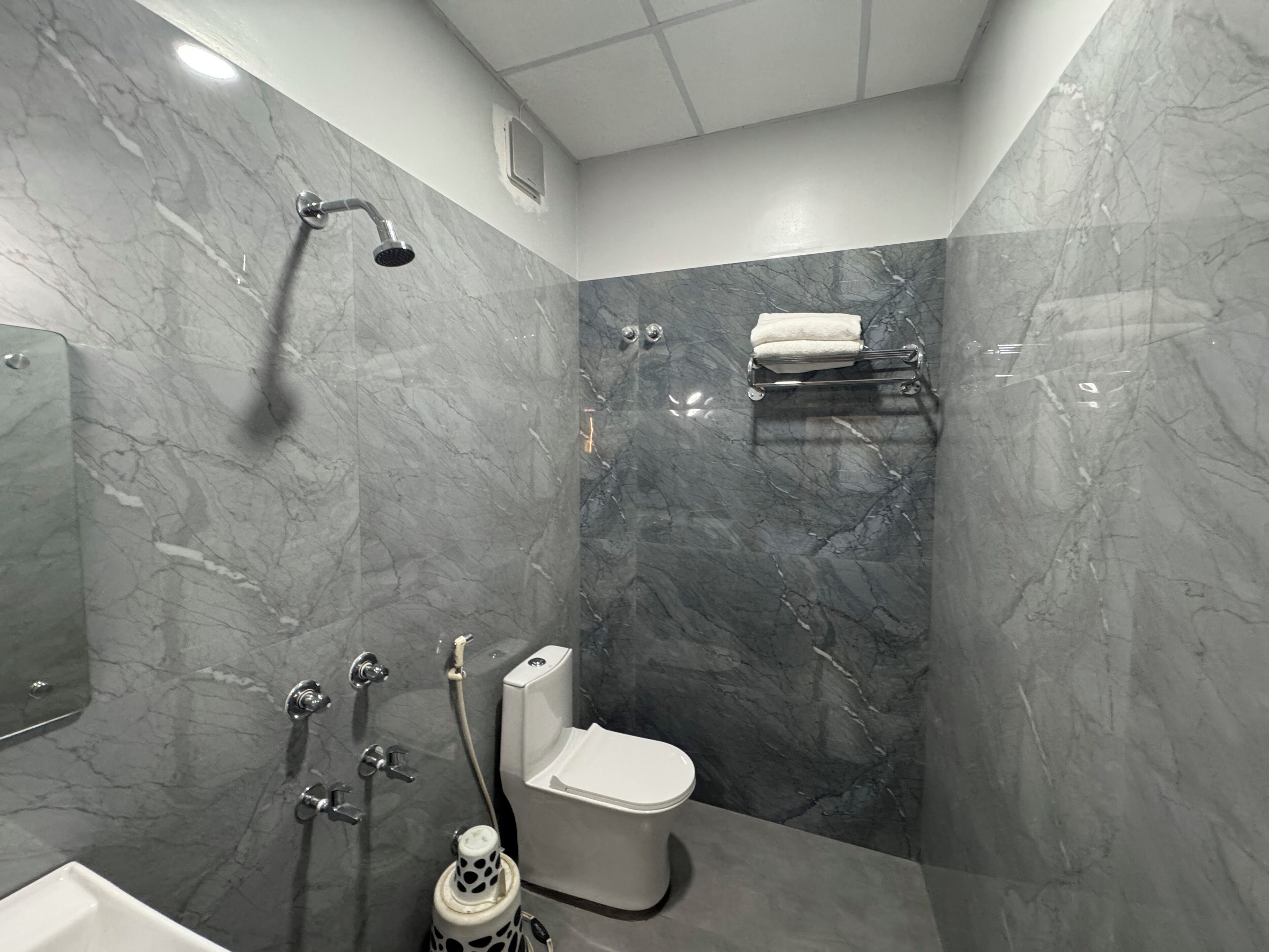 Un baño moderno con ducha, inodoro y lavamanos, todo con paredes de mármol.