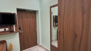 Una habitación con televisión montada en la pared, un armario de madera, una silla y piso de baldosas.