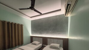 Une chambre d’hôtel avec deux lits simples, un ventilateur de plafond, un appareil de climatisation et une grande fenêtre avec des rideaux.