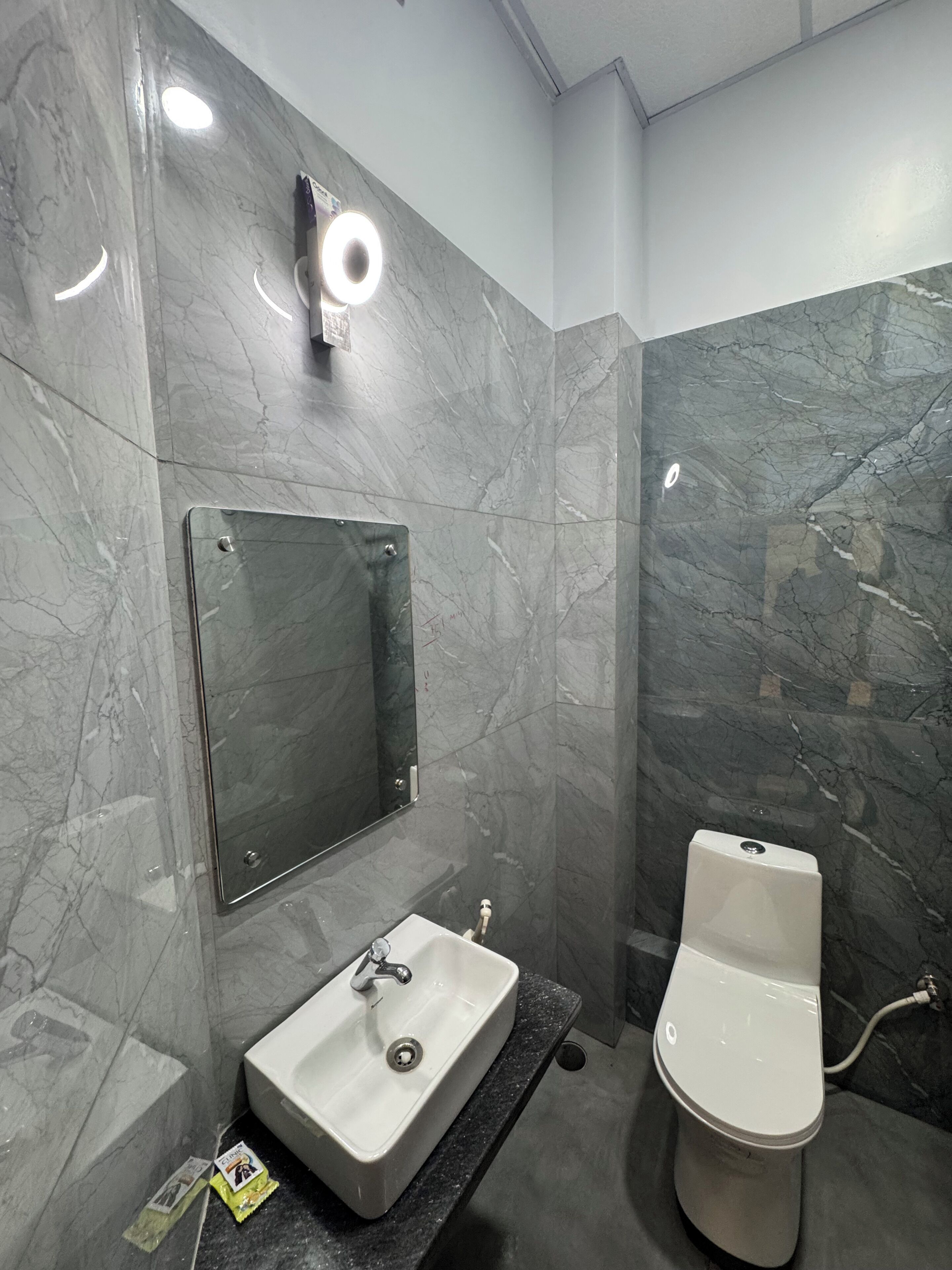 A bathroom with a marble wall, a sink, a toilet, and a mirror.
