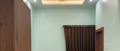 A bedroom with a bed, wooden wardrobe, ceiling fan, and a window with curtains.