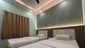 Une chambre d’hôtel avec deux lits simples, un ventilateur de plafond, des spots encastrés et un rideau à la fenêtre.