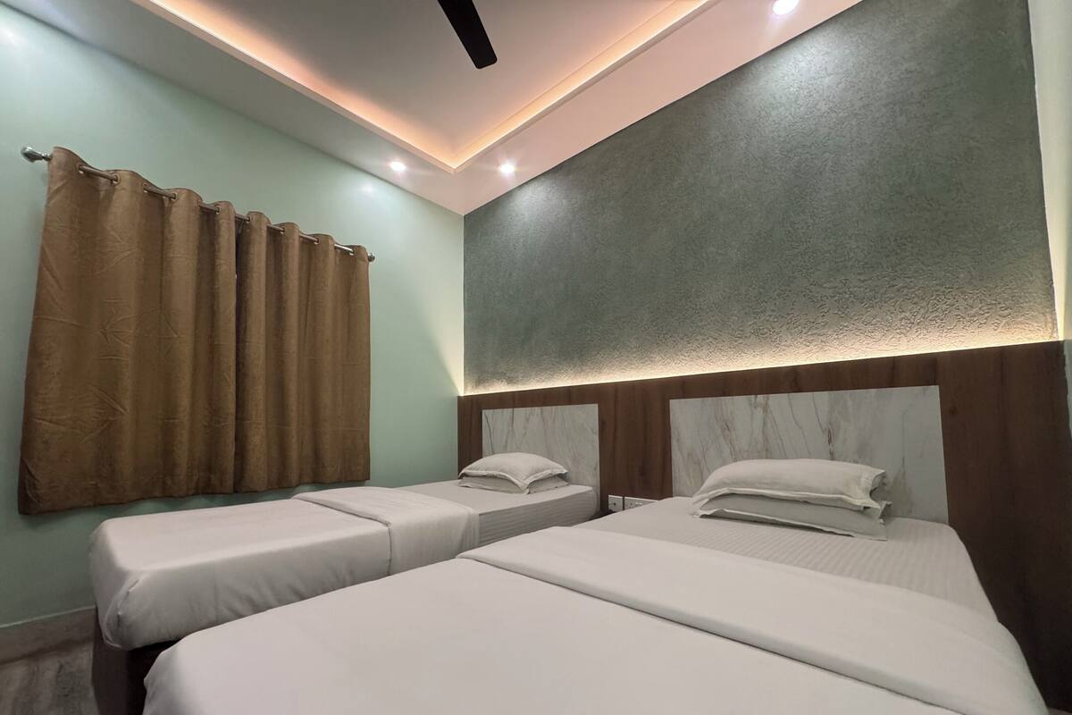 A hotel room with two single beds, a ceiling fan, recessed lighting, and a curtain on the window.