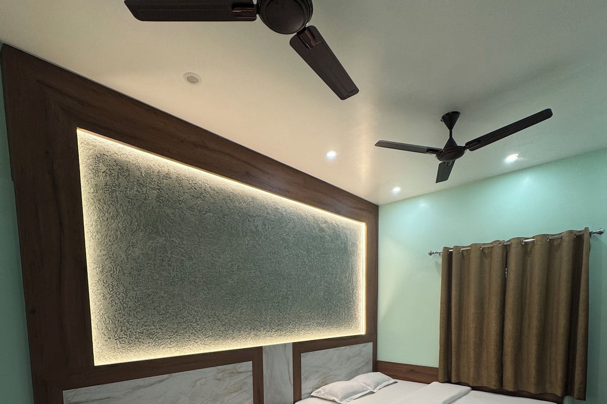 A hotel room with two beds, a ceiling fan, a wall-mounted light, and a curtain.