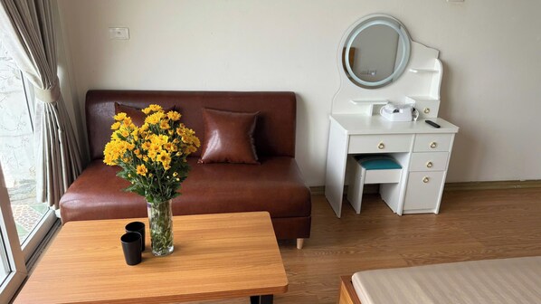 A hotel room with a brown leather sofa, a white desk with a mirror, a vase of yellow flowers, and a wooden table.