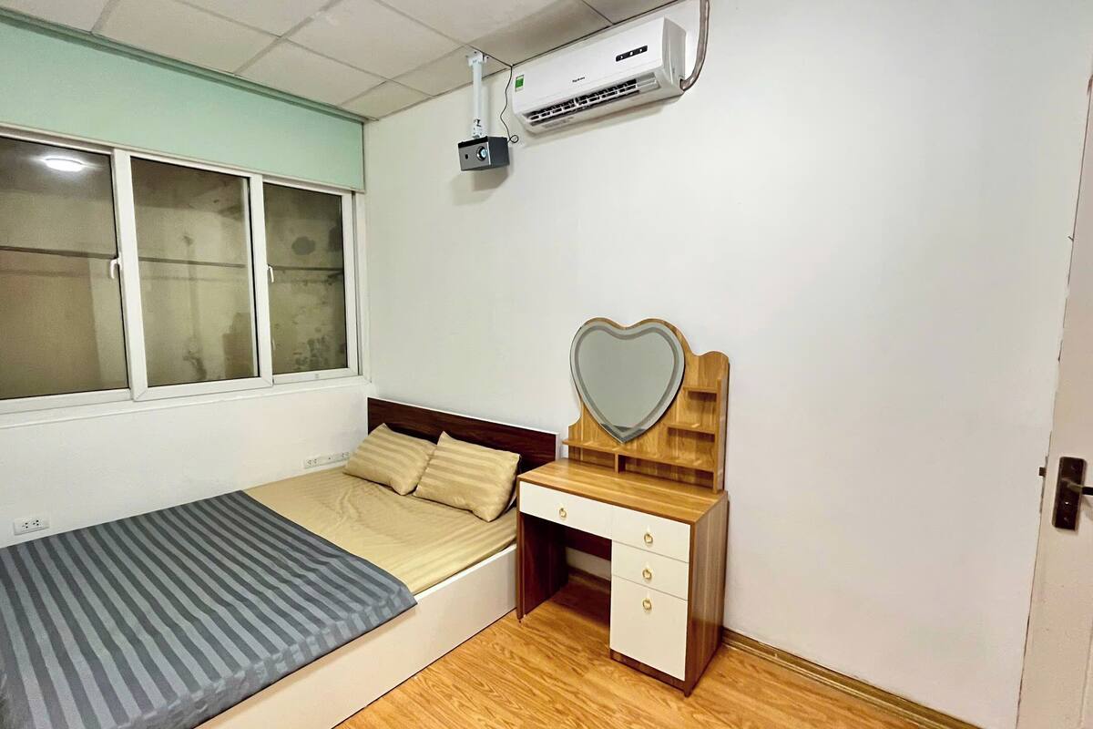 A bedroom with a bed, a dresser with a mirror, and an air conditioning unit above the bed.