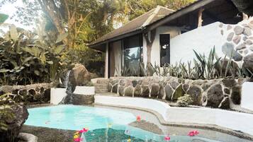 A pool with a waterfall, surrounded by tropical plants and a stone wall.
