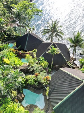 Ein Resort mit mehreren Schwimmbecken, umgeben von üppiger Vegetation und Palmen, mit Blick auf ein Gewässer.