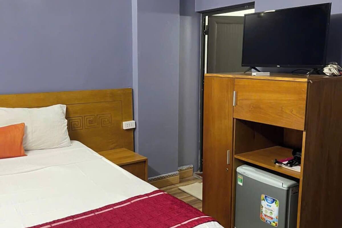 A hotel room with a bed, a television, a mini-fridge, and an air conditioning unit.