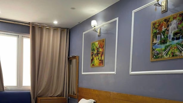 Ein Hotelzimmer mit zwei Betten, einem Fenster mit Vorhängen und zwei an der Wand befestigten Bildern.