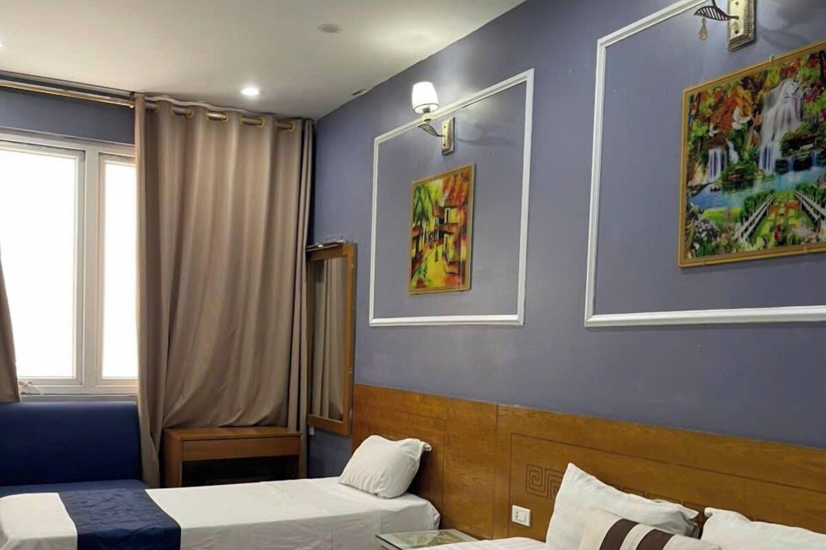 A hotel room with two beds, a window with curtains, and two wall-mounted paintings.