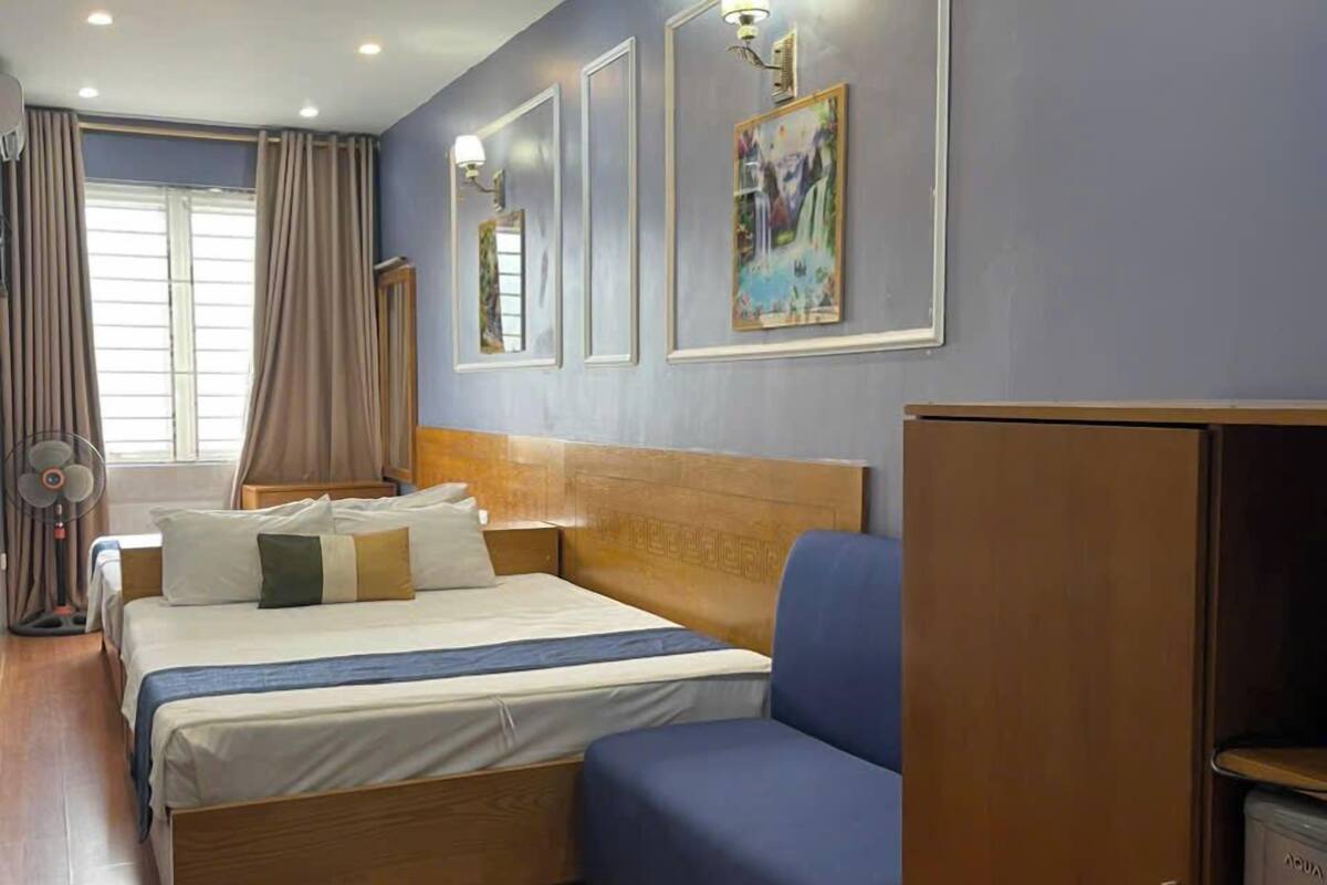 A hotel room with a bed, a blue sofa, a wooden wardrobe, and a window with curtains.