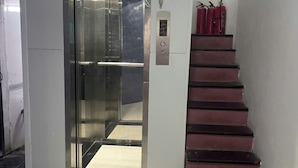 Ein Aufzug mit Glastür, ein Feuerlöscher an der Wand und eine Treppe mit roten Stufen.