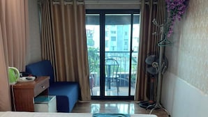 Ein Hotelzimmer mit Bett, Schreibtisch, Stuhl und einem Balkon mit Blick auf Gebäude, sowie einer Klimaanlage.
