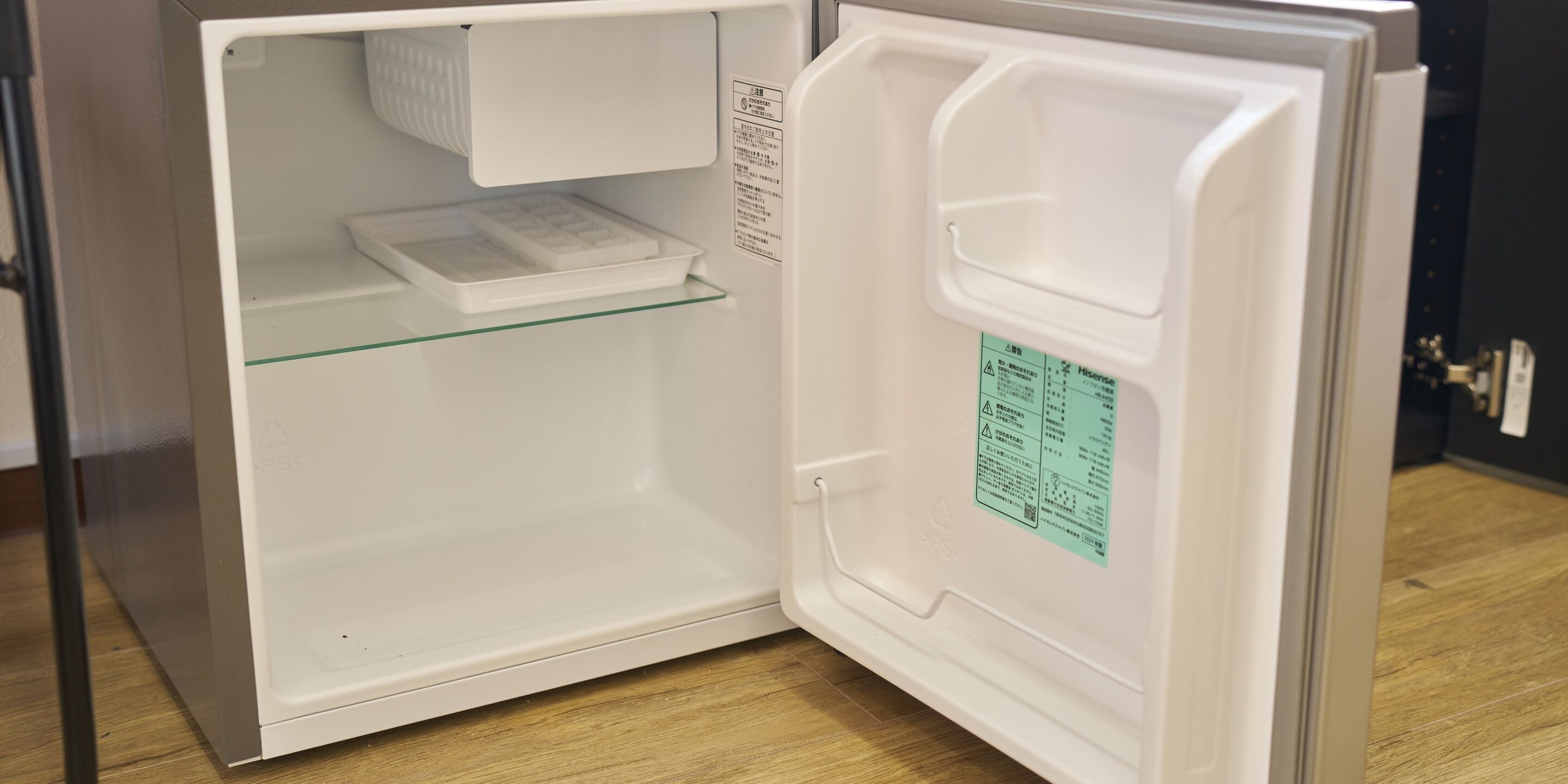 An open refrigerator with a glass shelf and a warning label.