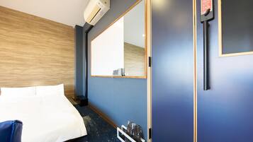 Una habitación de hotel con cama, un espejo grande, un armario y un equipo de aire acondicionado.