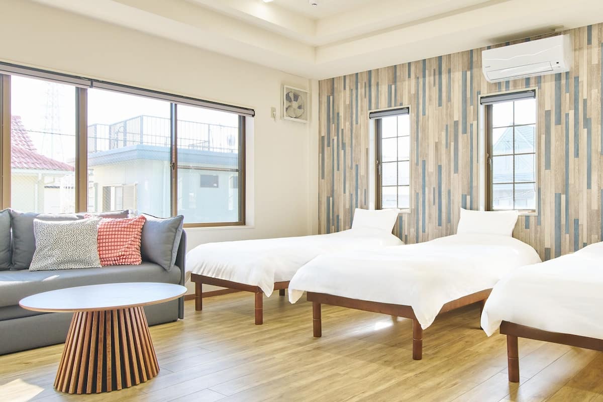 A hotel room with two beds, a sofa, a round wooden table, and large windows.