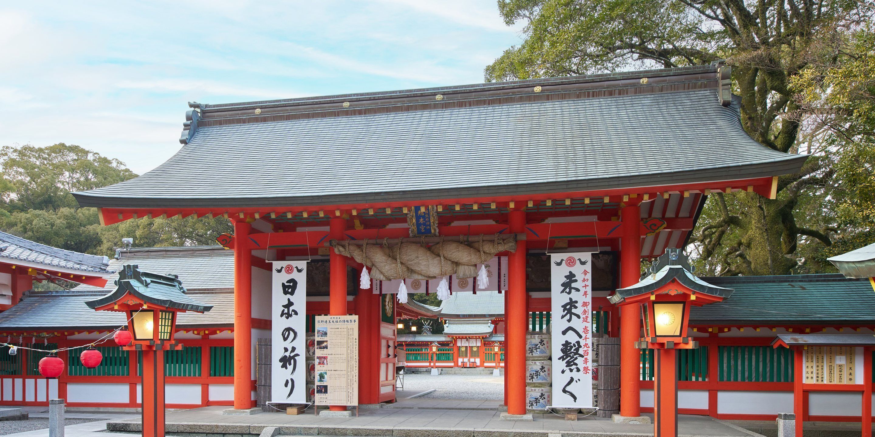 Un templo japonés tradicional con un torii rojo, faroles y señalización en japonés.