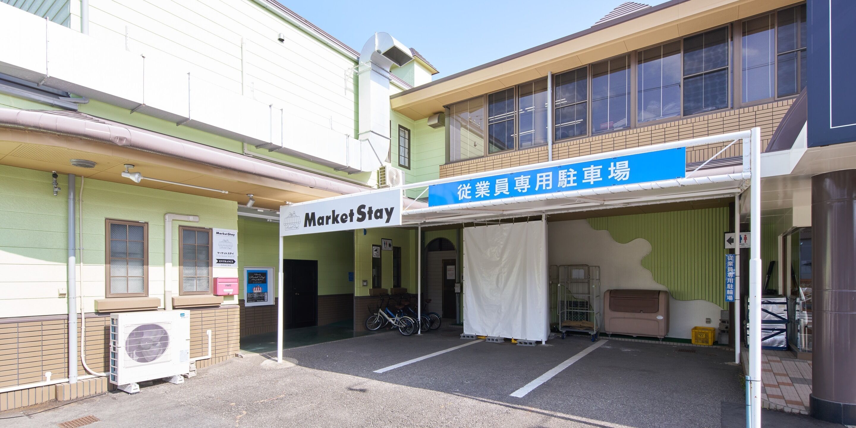 A building with a MarketStay sign, a covered parking area, and a bicycle parked outside.