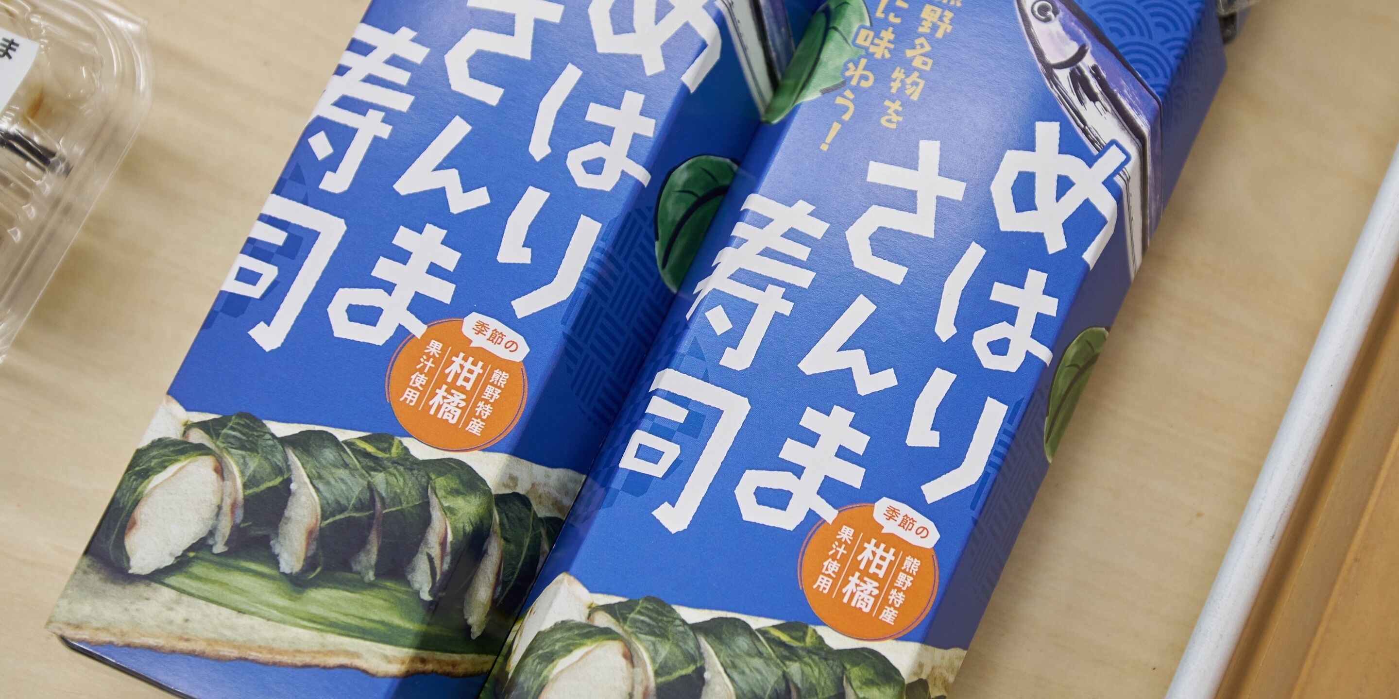 Twee sushi-verpakkingen met Japanse tekst en afbeeldingen van sushirollen.