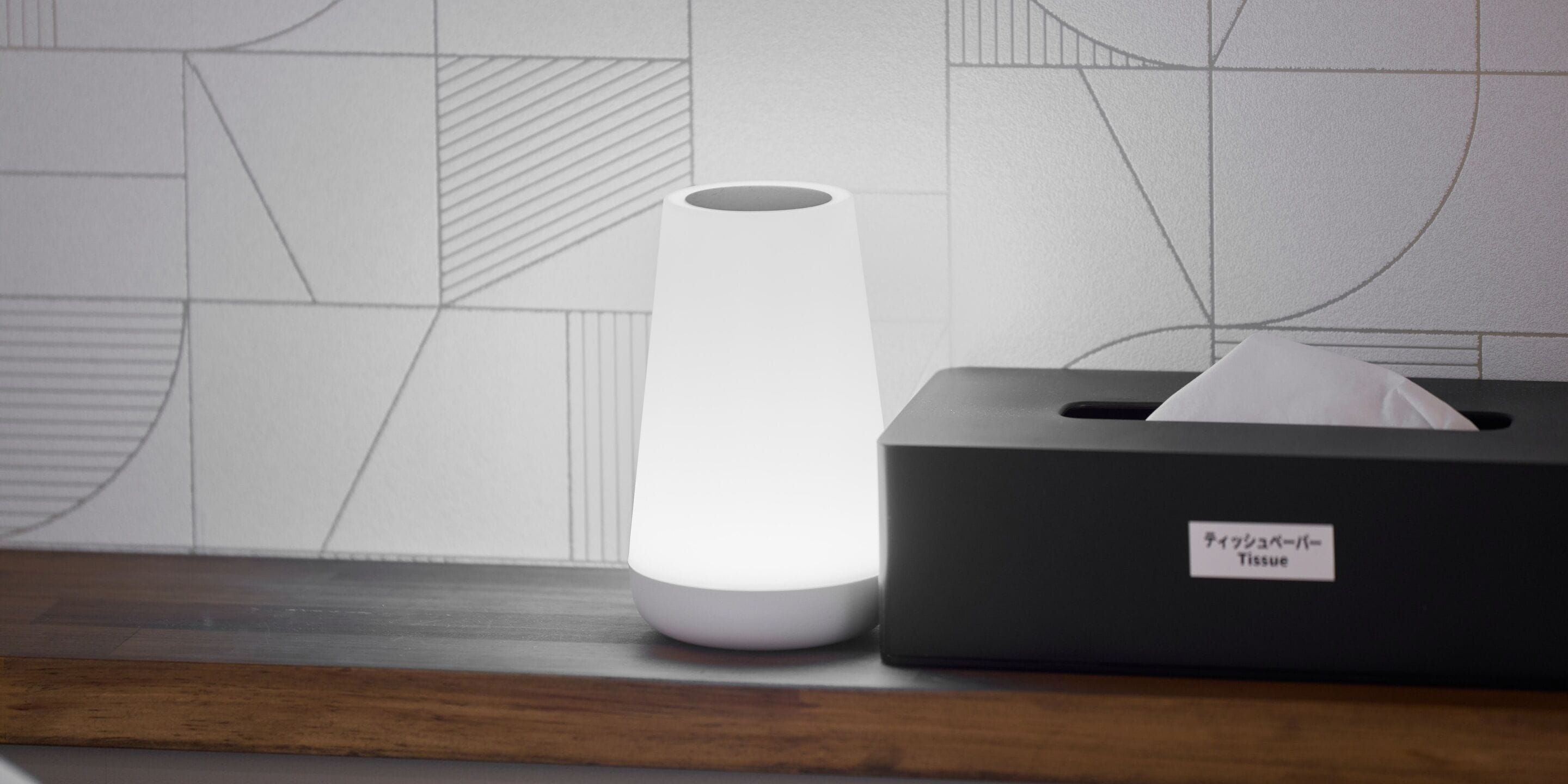 A tissue box and a white cylindrical object on a wooden surface against a tiled wall.