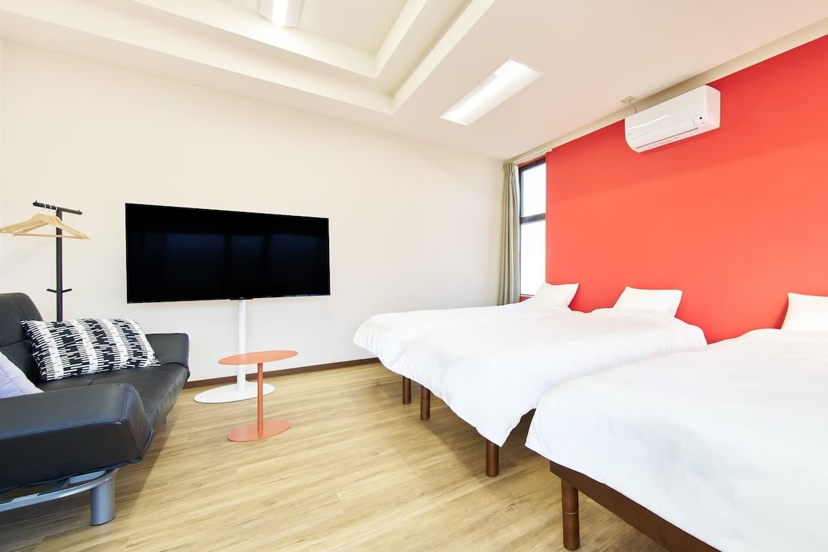 A hotel room with two beds, a TV, a desk, and a red accent wall.