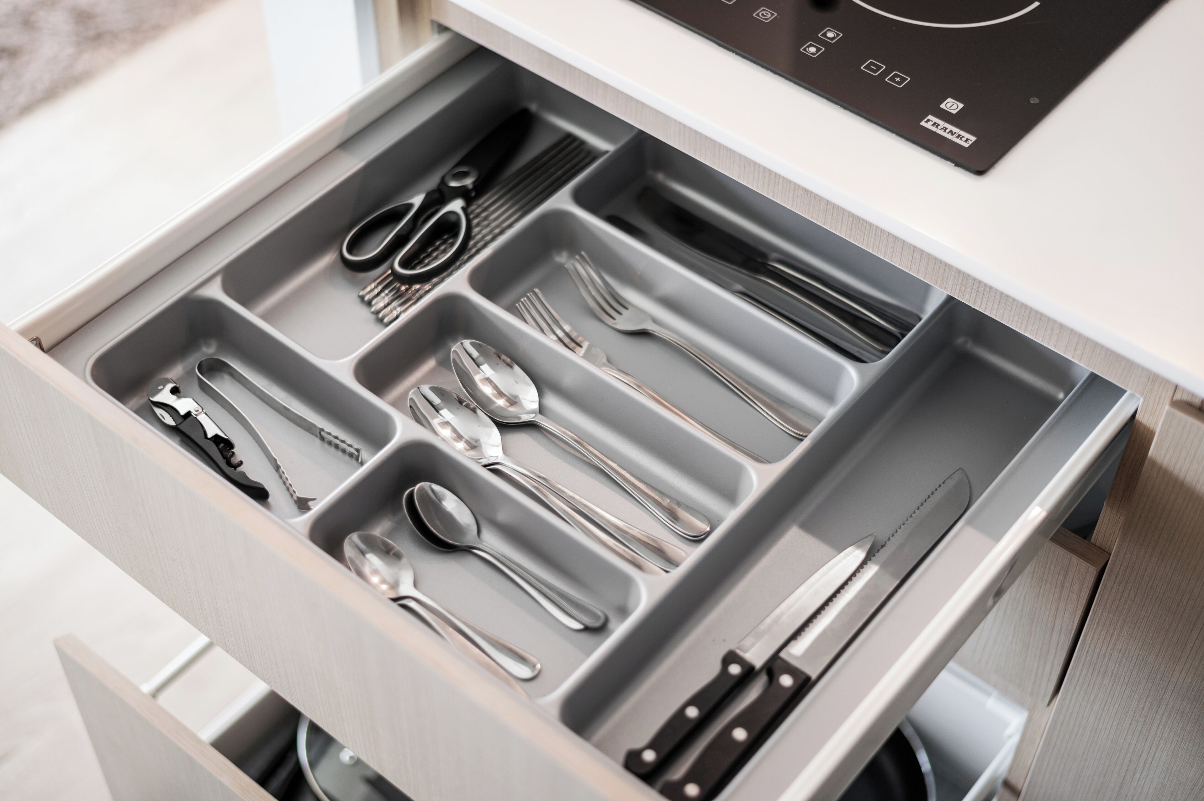 Un cajón con divisiones que contiene varios utensilios de cocina como cuchillos, cucharas, tenedores y un par de tijeras.