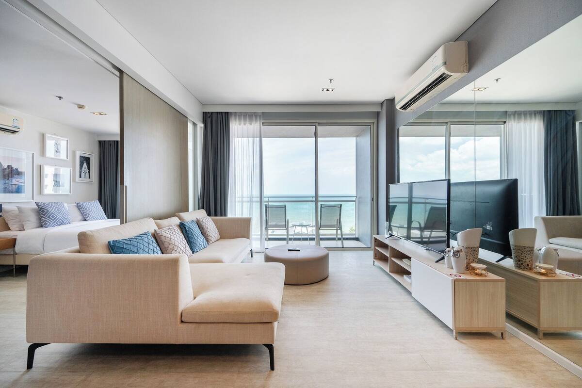 A modern hotel room with a bed, sofa, TV, and a balcony with a view.