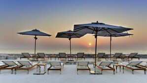 A beachside lounge area with sun loungers and umbrellas, overlooking the ocean at sunset. - Veranda Residence by SEA U PATTAYA (Pattaya)