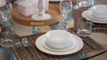 A dining table set with white plates, bowls, and cutlery, a glass vase, and a tray with a white object.