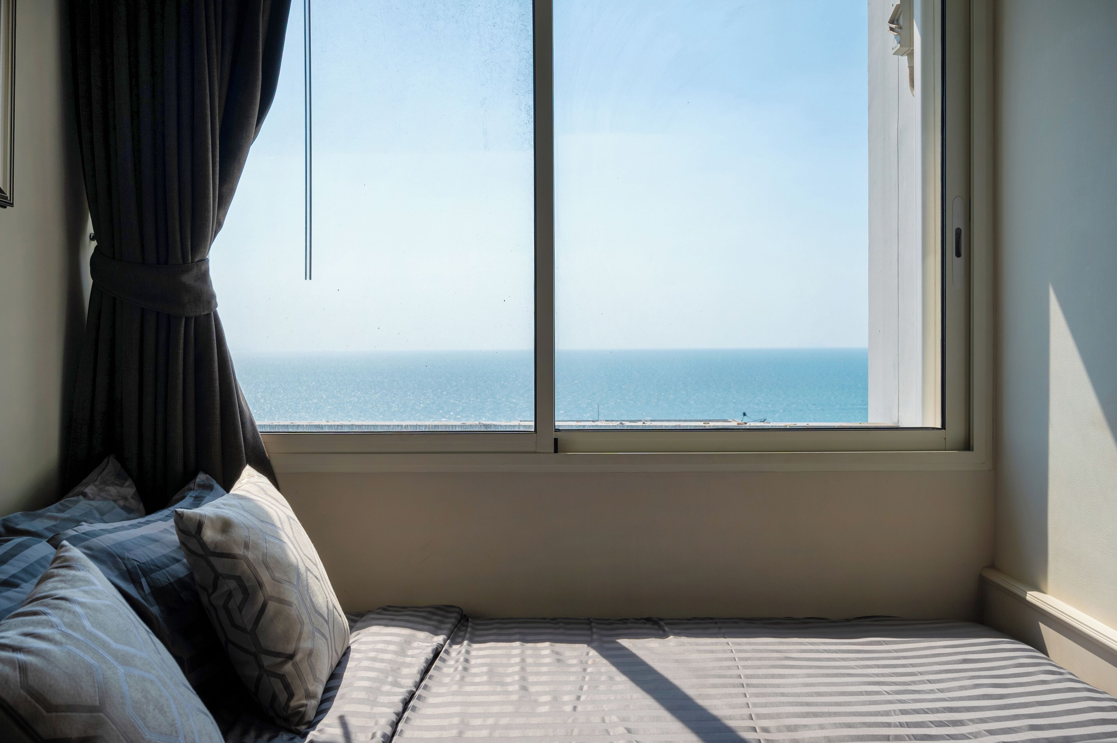 Une chambre avec un lit, une fenêtre avec des rideaux et une vue sur la mer.