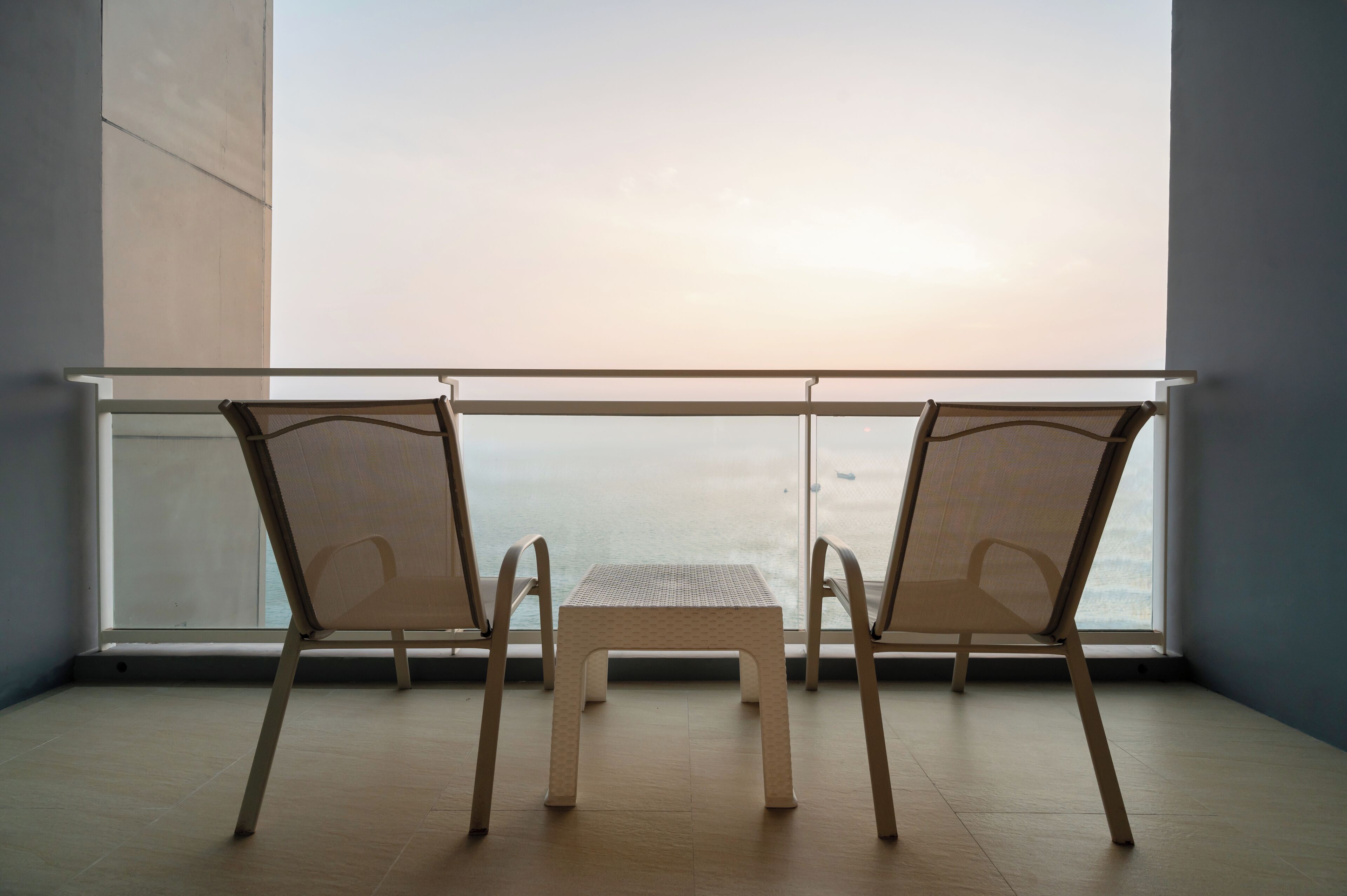 A balcony with two chairs and a small table, overlooking a body of water.