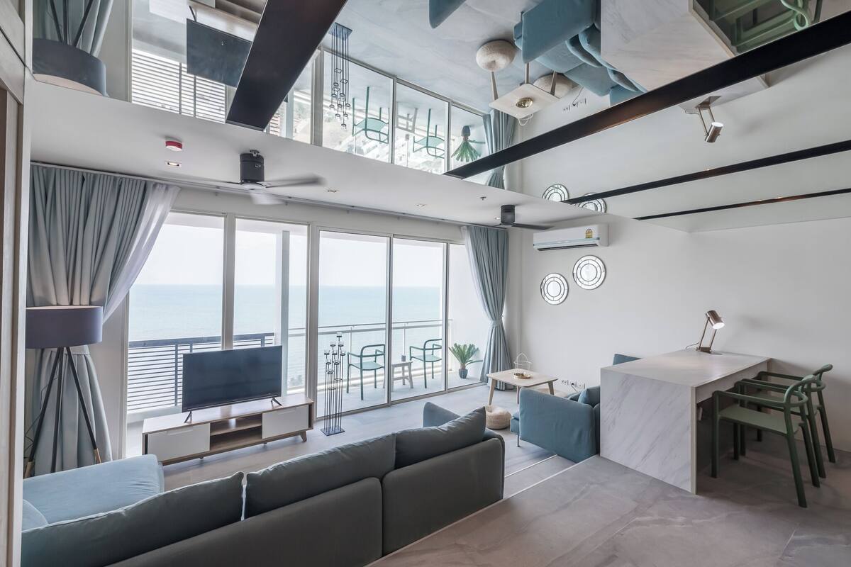 A modern living room with a large window, a sofa, a dining table, and a TV.