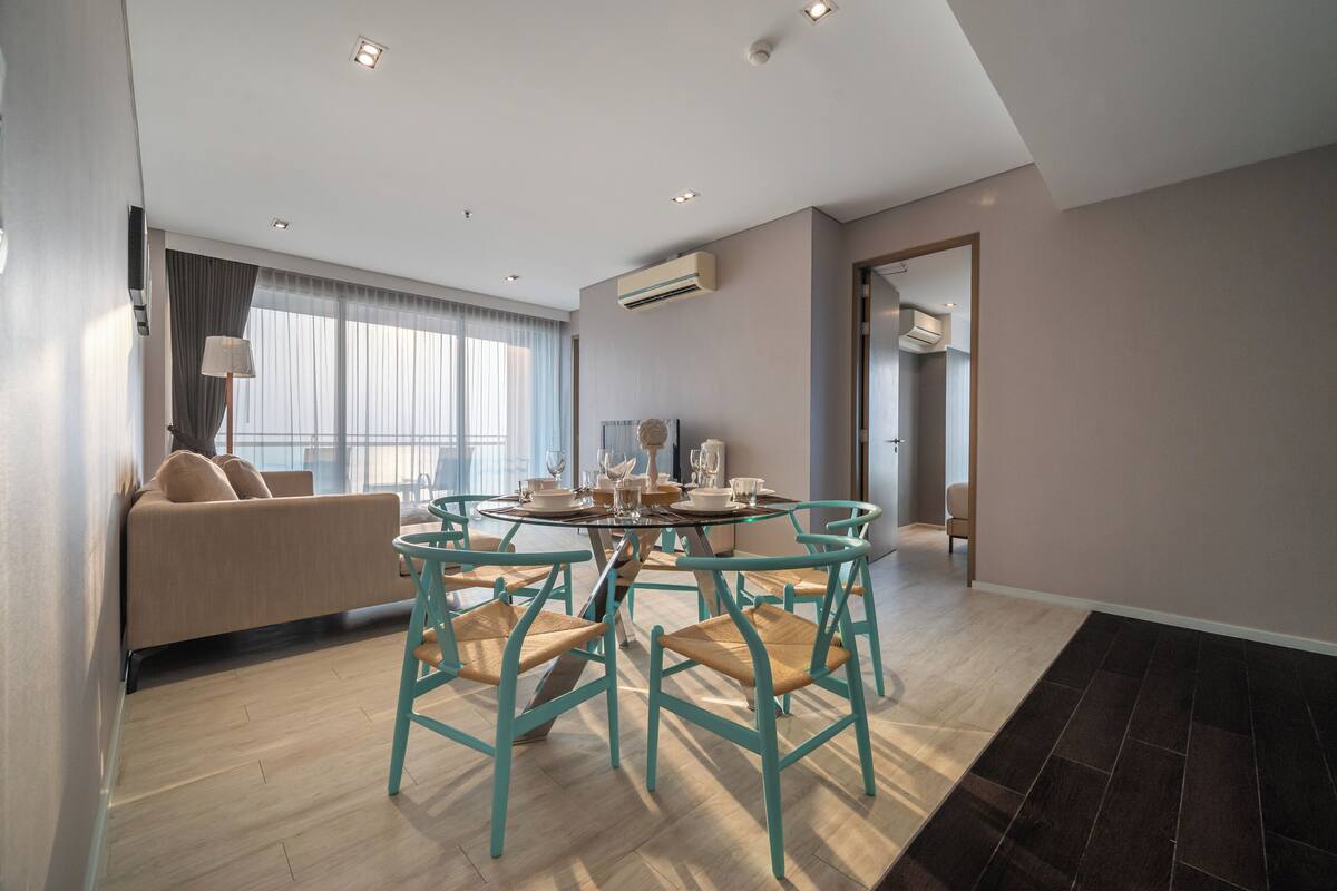 A modern living room with a sofa, a round dining table with chairs, and a large window with curtains.