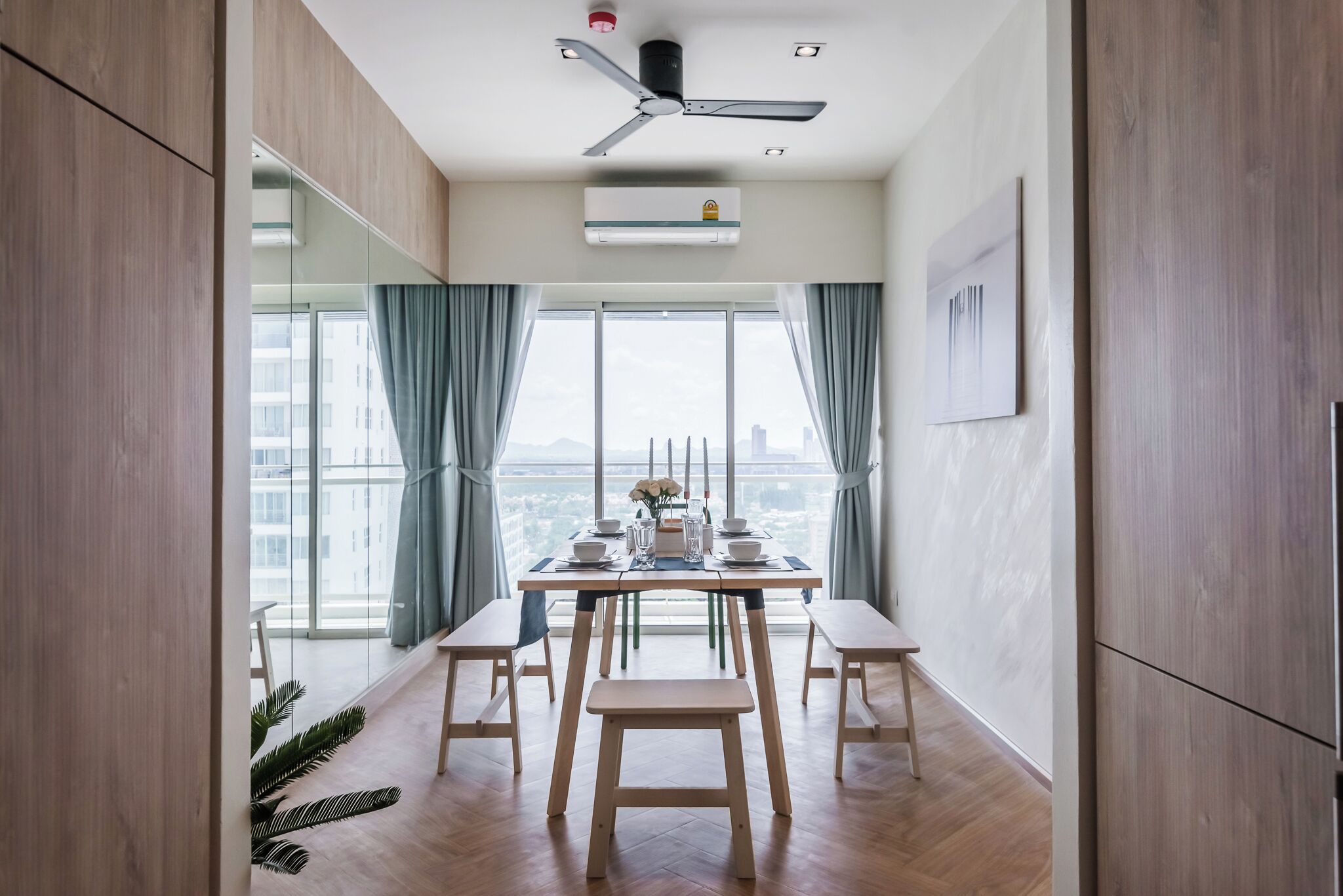 Ein moderner Essbereich mit Deckenventilator, einem mit Stühlen gedeckten Esstisch und Blick auf die Stadt durch große Fenster.