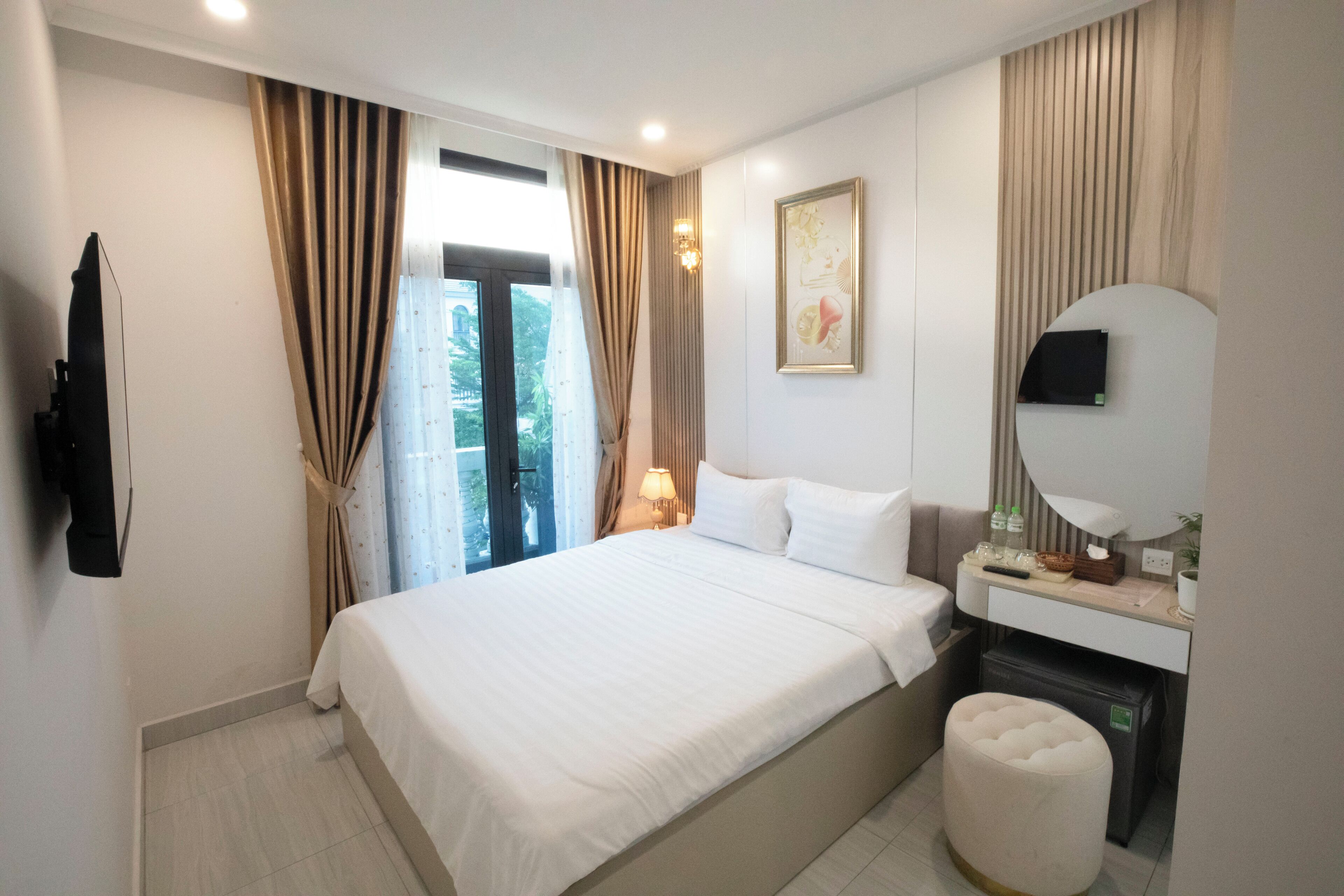Habitación de hotel con cama, escritorio con espejo, televisor montado en la pared y ventana con cortinas.