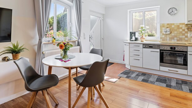 A modern kitchen with a dining area, featuring a round table with chairs, a coffee maker, and a clock on the wall. - Holiday apartment near the beach with a terrace (Hohenkirchen OT Wahrstorf)