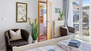 A bedroom with a bed, two chairs, a radiator, a window with curtains, a door leading to a balcony, and a small table with a teddy bear and flowers. - Holiday apartment near the beach with a terrace (Hohenkirchen OT Wahrstorf)