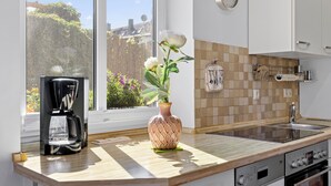 A modern kitchen with a coffee maker, a vase with flowers, and a view of greenery outside. - Holiday apartment near the beach with a terrace (Hohenkirchen OT Wahrstorf)