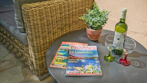 Une chaise en osier, une table avec une bouteille de vin, deux verres et un magazine intitulé « PROVENCE ».