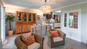 Un salon spacieux, meublé de meubles en osier, avec un buffet en bois et un coin repas comprenant une table et des chaises blanches.