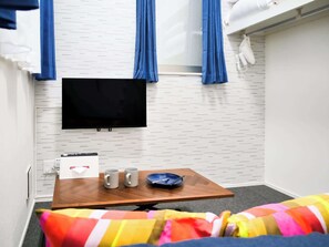 Una habitación con una televisión de pantalla plana, una mesa de madera con dos tazas, un plato y una manta a rayas colorida.