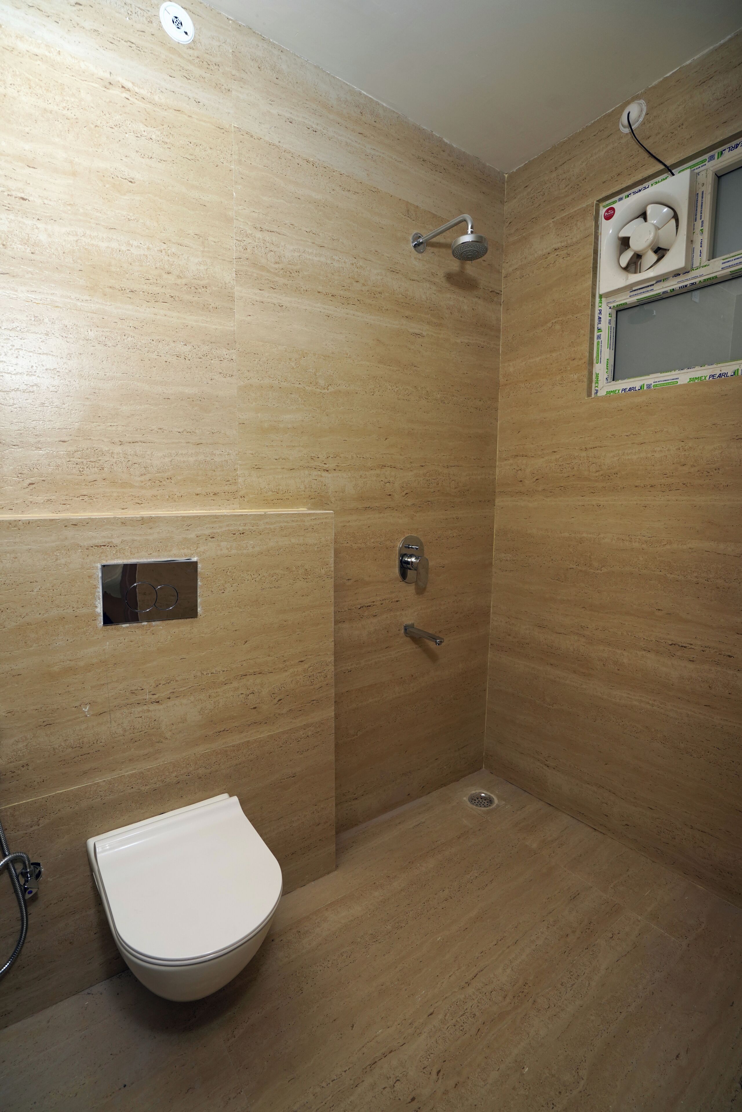 A bathroom with a shower, toilet, and a fan mounted on the wall.