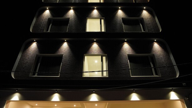 Un immeuble à plusieurs étages, doté de fenêtres illuminées et d’un balcon au niveau du rez-de-chaussée.