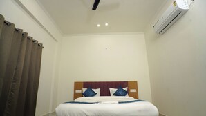 Une chambre d’hôtel avec un lit, des rideaux, un appareil de climatisation et un luminaire au plafond.