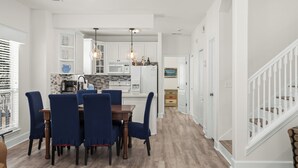A modern kitchen with white cabinets, a dining table with blue chairs, and a staircase with white railings. - 10 min. Walk to Beach - Close to Pool - 4 Bikes (Santa Rosa Beach)