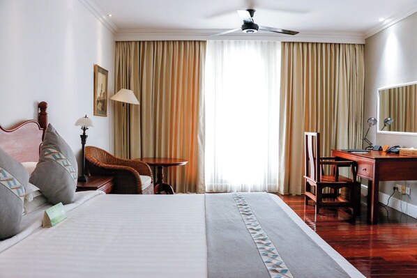 A hotel room with a bed, a desk, a chair, a lamp, and a large window with curtains. - Hotel Boundary (Yangon)