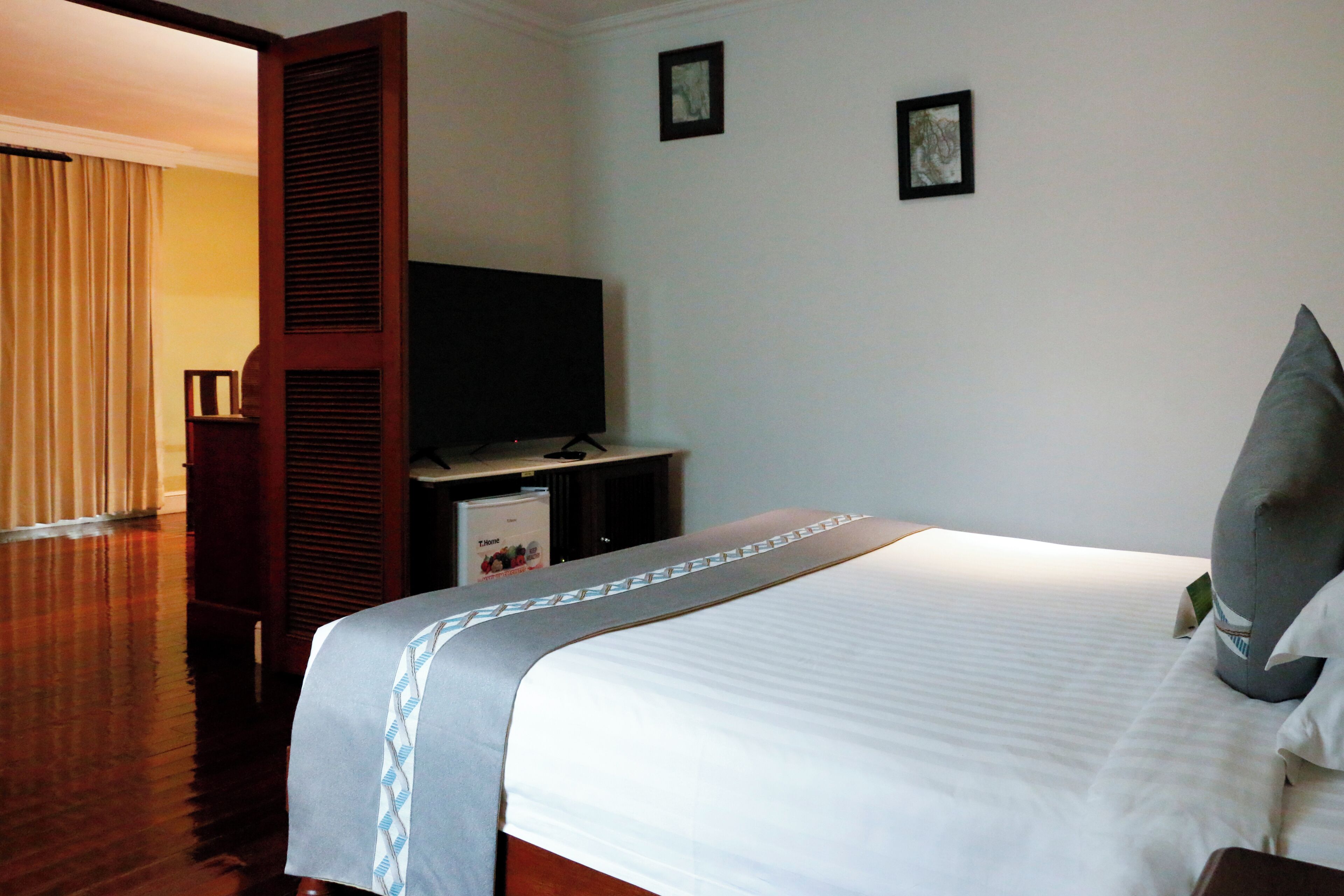 Habitación de hotel con una cama grande, un televisor sobre un mueble y una puerta que da a otra habitación.
