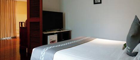 Habitación de hotel con una cama grande, un televisor sobre un mueble y una puerta que da a otra habitación.